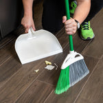 Person using a Libman green-handled angle broom to sweep debris into a white dustpan on wood floor
