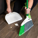 Person using a Libman angled broom with green bristles to sweep debris into a white dustpan