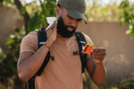 Person outdoors using a Ben's individual wipe packet, holding the orange sachet while wiping their neck with the wipe