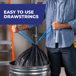 Lifestyle image of a person pulling blue drawstrings to close a full black Hefty trash bag over a metal can with 'easy to use drawstrings' callout
