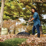 Person raking a pile of leaves in a park using a Fiskars leaf rake, with a collapsible leaf bag nearby