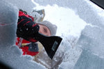 Person using a black ice scraper to clear snow and ice from a car window, viewed through the partially cleared windshield.