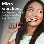 Lifestyle image of a person holding a black Philips One by Sonicare toothbrush near their teeth with micro vibrations text.