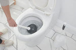 Person using a black-cupped plunger in a white toilet bowl with the toilet seat raised in a tiled bathroom scene