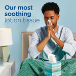 Person seated on bed using a Puffs tissue from a cube on the blanket with 'Our most soothing lotion tissue' text
