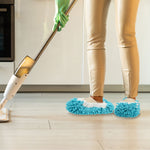 Lifestyle shot of a person wearing blue chenille mop slippers while mopping a light wood floor with a mop.