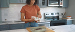 Kitchen lifestyle scene of a person wiping a casserole dish on a countertop with a dish towel