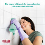Person wearing purple gloves wiping white tiled wall with a green cloth and headline 'The power of bleach for deep cleaning and stain-free surfaces'