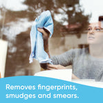 Person wiping a large window with a cloth, visible fingerprints on glass and cleaning action