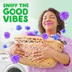 Smiling person holding a laundry basket with floating purple flowers and text Sniff the Good Vibes on a light green backdrop