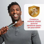 Smiling person holding a toothbrush with a gold shield icon and text describing a mineral shield for sensitive spots