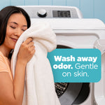 Person holding a soft white towel near an open washing machine with text reading “Wash away odor. Gentle on skin.”