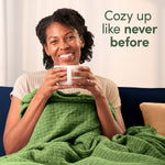 Smiling person wrapped in a green textured blanket holding a mug with copy reading cozy up like never before