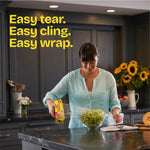 Person in kitchen wrapping a bowl of grapes with Glad Cling'N Seal film, boxed product in hand and text promoting easy tear and cling
