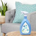 Great Value blue spray bottle of Pet Odor Eliminator displayed on a wooden table with a couch and cushion in the background