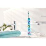 Turquoise Philips Sonicare kids electric toothbrush standing upright on a sink countertop in soft bathroom lighting.