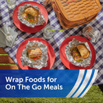 Picnic table setting with sandwiches wrapped in aluminum foil on red plates and a picnic basket, showing foil used for on-the-go meals