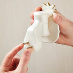 Close-up of hands holding a white pineapple plug-in diffuser while pointing at the metal plug prongs on the back of the unit.