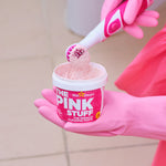 Close-up of hands in pink gloves holding open tub of The Pink Stuff cleaning paste and applying with brush