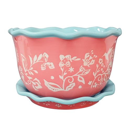 Close-up of a coral ceramic planter with white floral pattern and aqua scalloped rim and saucer