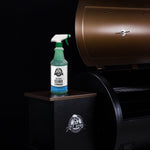 Pit Boss cleaner spray bottle placed on a side shelf next to a brown grill against dark background