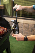 Two hands operating the pump mechanism on a Pit Boss spritzer bottle next to a closed grill