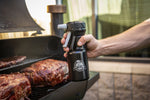 Hand holding Pit Boss spritzer bottle near a grill with smoked roasts visible on the grate