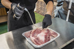 Person wearing gloves using Pit Boss spritzer and injector to inject liquid into a large piece of meat in a pan
