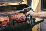 Hand spraying mist from a Pit Boss spritzer bottle over roasts on a grill