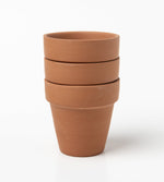 Three stacked unpainted terra cotta pots photographed on a white background, showing worn surface texture