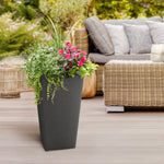Black tapered planter styled on a deck with flowering plants and wicker patio furniture in the background
