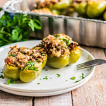 Plated stuffed bell peppers in front of a disposable aluminum baking pan on a wooden surface