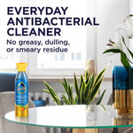 Pledge multisurface cleaner bottle placed on a glass table in a bright living room setting with product claim text
