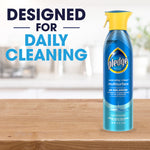 Pledge multisurface spray bottle on a wooden surface with blurred kitchen background and bold text 'DESIGNED FOR DAILY CLEANING'.