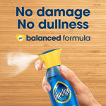 Close-up of a hand holding a Pledge spray bottle, mist coming from the nozzle, text above reads 'No damage No dullness balanced formula'.