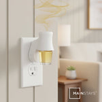 Wall plug fragrance diffuser inserted into outlet with a small glass oil bottle attached and scented vapor rising in a living room setting.