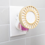 Plug-in diffuser inserted in a wall outlet with a pink glass fragrance refill bottle attached beneath a decorative vented cover