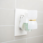 Plug-in fragrance warmer inserted in wall outlet holding a small glass oil refill with pale green liquid