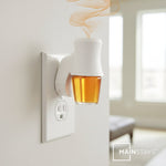 Wall outlet plug-in warmer with amber fragrance oil refill bottle inserted, releasing visible scented vapor