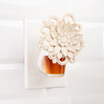 Decorative wall plug-in warmer holding an amber fragrance oil refill bottle against a tiled white wall