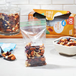 Kitchen scene with a filled clear Portion Snack Bag in front, box packaging and bowls of nuts in the background
