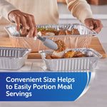 Person portioning roasted meat and potatoes into a small aluminum tray from a larger foil pan using tongs