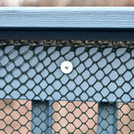 Close-up of green plastic poultry netting attached to a painted wooden railing with a visible screw fastener