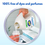 Hand pouring liquid from an all free•clear fabric softener bottle into a measuring cap over towels