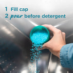 Hand pouring bright blue scent crystals from a measuring cap into the drum of a washing machine with usage instructions visible.