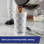 Coffee being poured into a Hefty gray lattice-pattern disposable cup with lids and napkin on a countertop