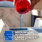 Close-up of blue liquid detergent being poured from a red cap into a washer dispenser with dosing guide overlay