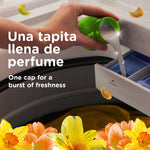 Hand pouring Downy fabric softener from a green cap into a washer softener dispenser with floral graphics