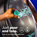 Hand pouring turquoise scent booster beads from a measuring cup into a washing machine drum