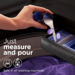 Hand pouring white liquid fabric softener into a washing machine dispenser with on-image text instructing to measure and pour